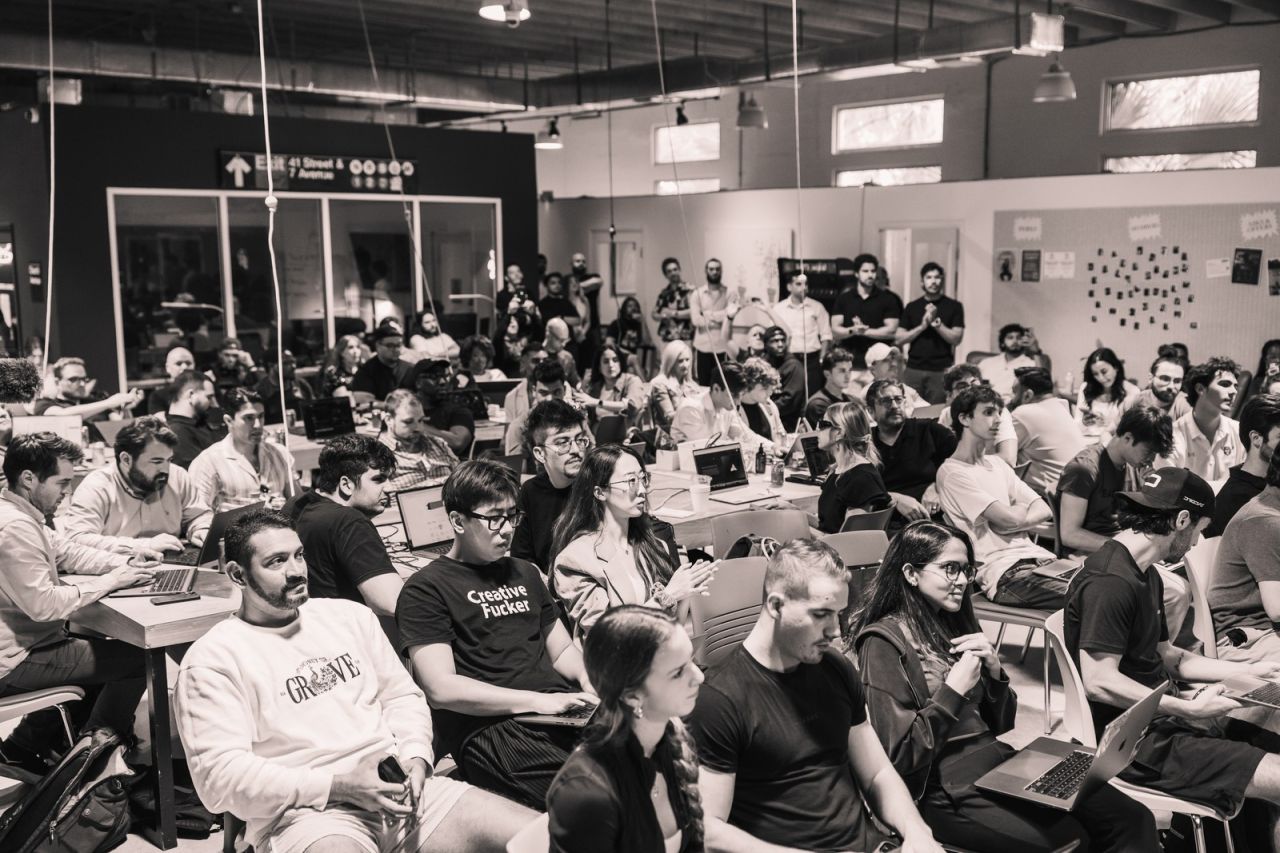 Black and white photograph of the full room of builders seated with laptops